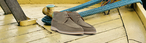 A pair of taupe suede casual shoes resting on a yellow wooden deck next to a blue rope.