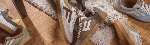 A pair of white and brown Floris van Bommel sneakers with red side stripes, displayed on a wooden floor next to a shag rug.