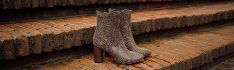 A pair of textured brown Floris van Bommel ankle boots with chunky block heels, resting on rustic red brick steps.
