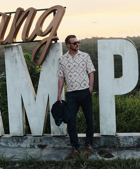 Floris van Bommel, wearing a short-sleeve button-up shirt with a pink and green trellis pattern, dark trousers, and sunglasses.